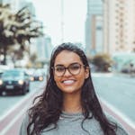 A young woman with glasses smiling on a city street, embracing urban lifestyle.