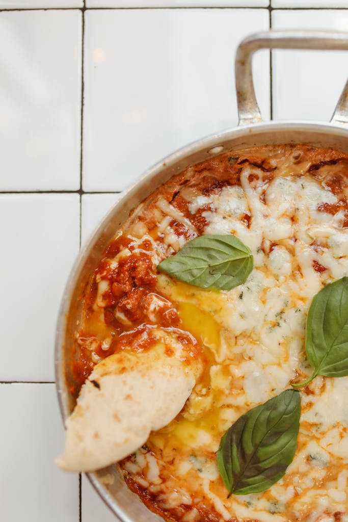 Close-up of delicious shakshuka topped with basil leaves in a skillet on a tile background.