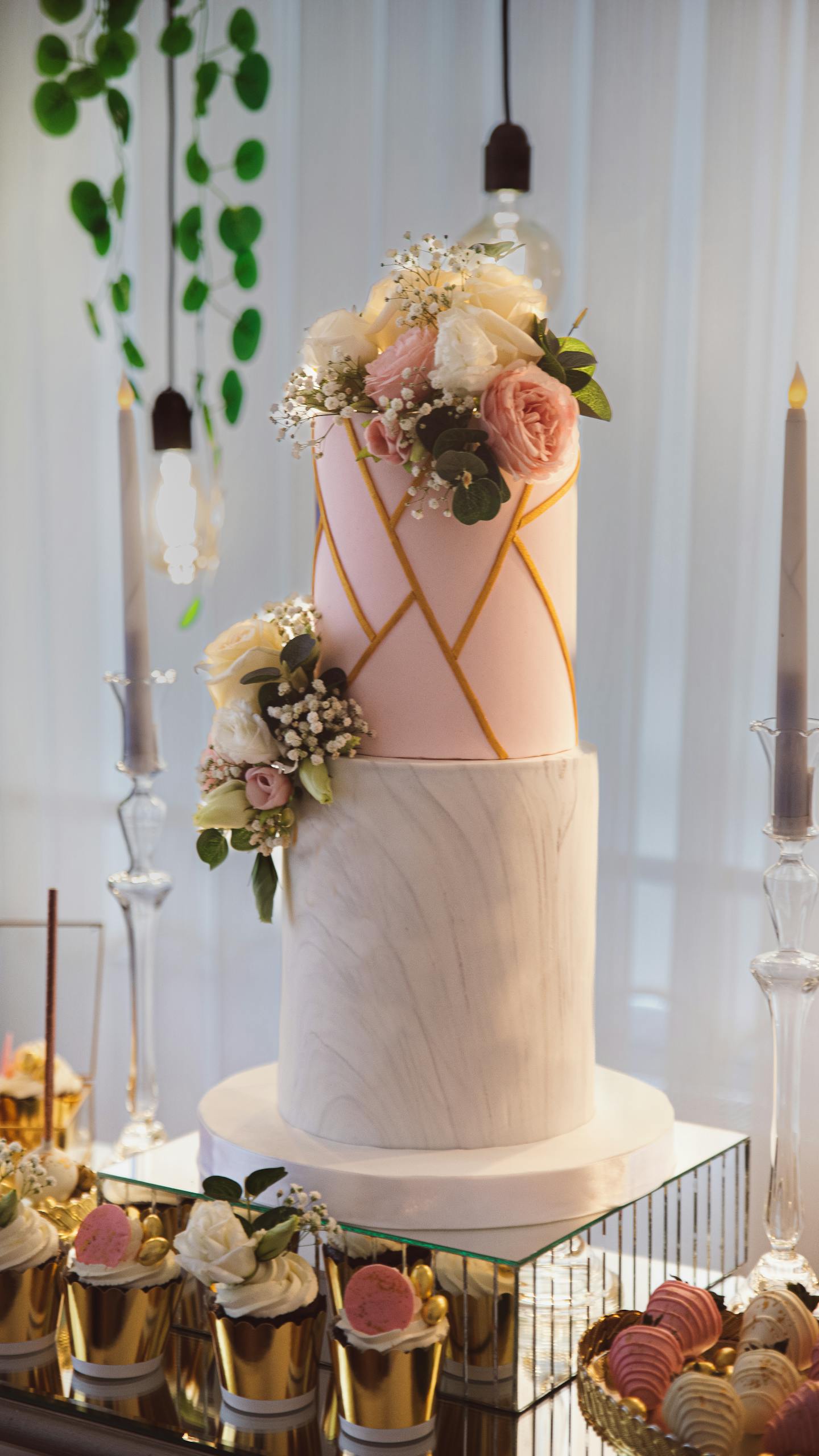Sophisticated two-tier wedding cake adorned with flowers, surrounded by candles and desserts.
